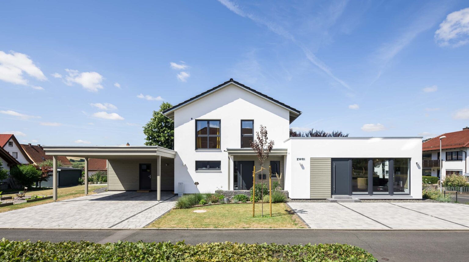 Einfamilienhaus als Holzrahmenbau mit Satteldach und Putzfassade und großem Carport