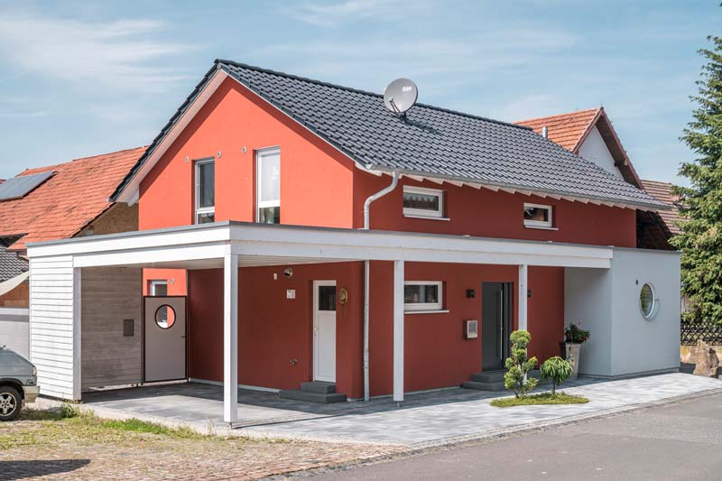 Einfamilienhaus aus Holz mit roter Putzfassade mit Carport